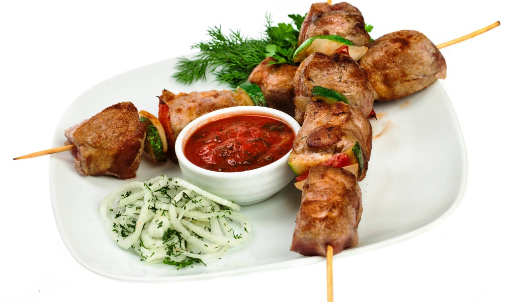 Шашлык на белой тарелке с соусом, зеленью и луком