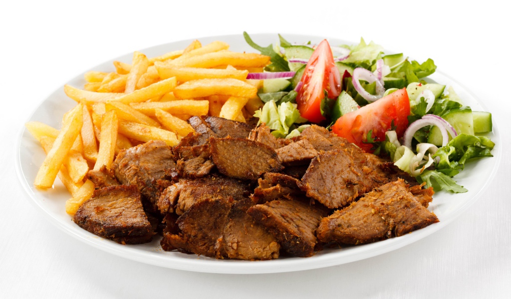 Кусочки мяса на тарелке с картофелем фри и салатом