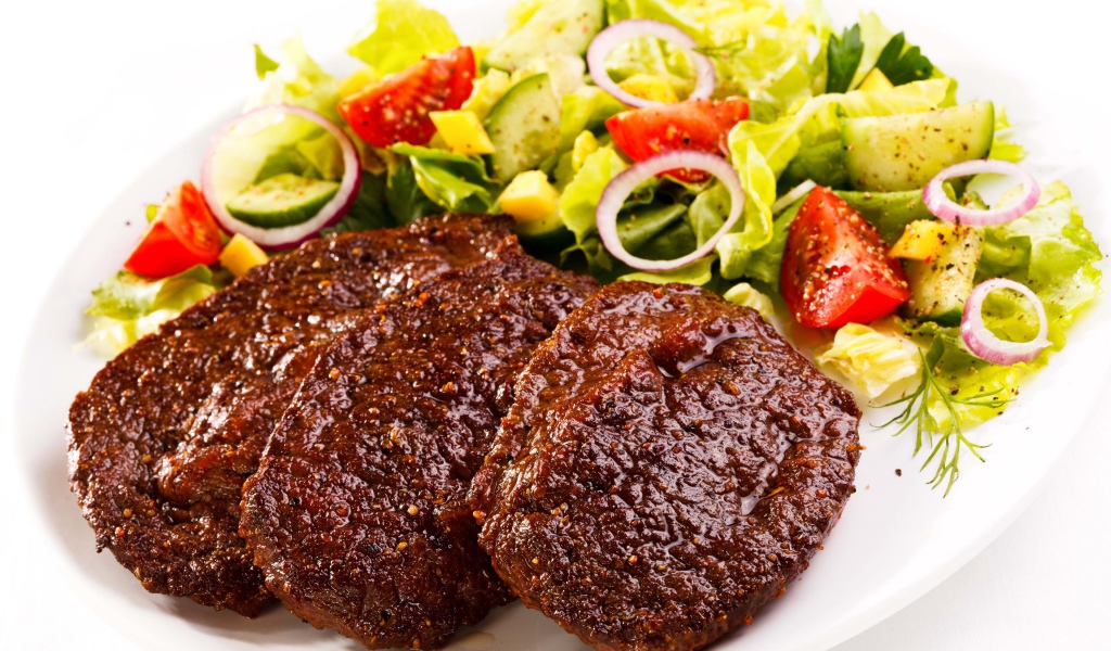 Три котлеты на тарелке с салатом на белом фоне