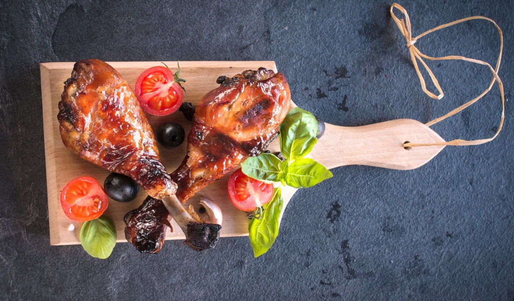 Две зажаренных куриных ножки с овощами на разделочной доске