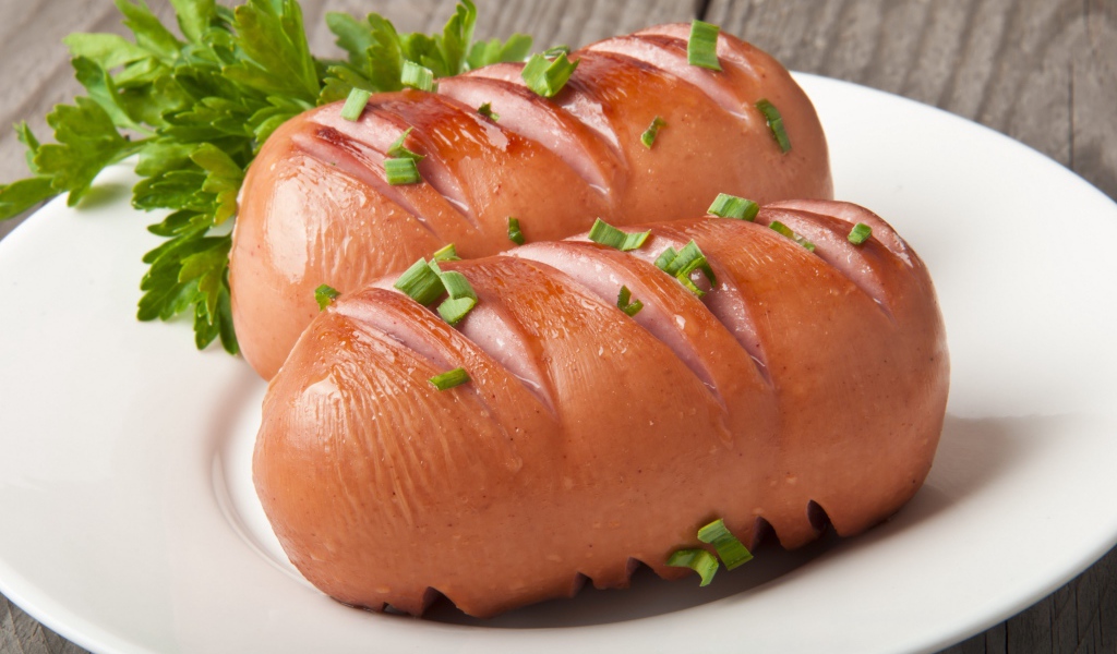 Два жареные сардельки на большой белой тарелке с зеленью 