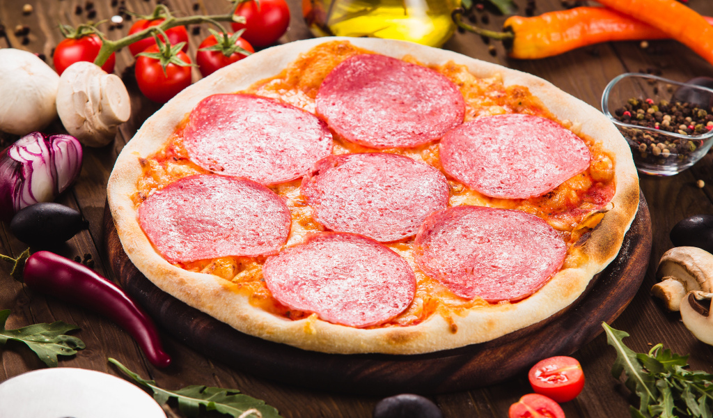 Пицца с салями на столе с овощами 