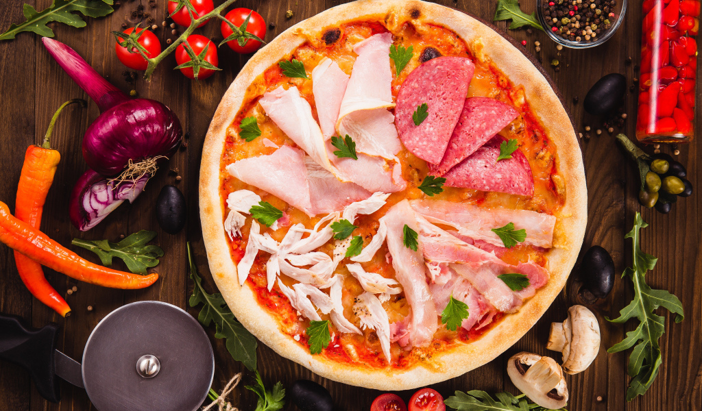 Пицца с колбасой, курицей и кусочками ветчины на столе с овощами 
