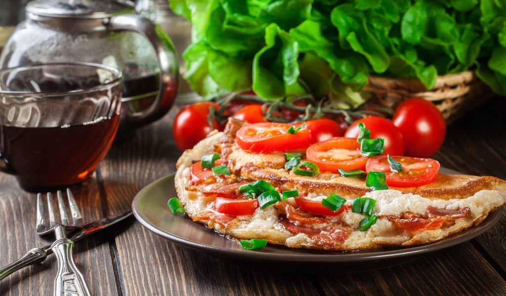 Пицца с помидорами на столе с чаем и зеленью 