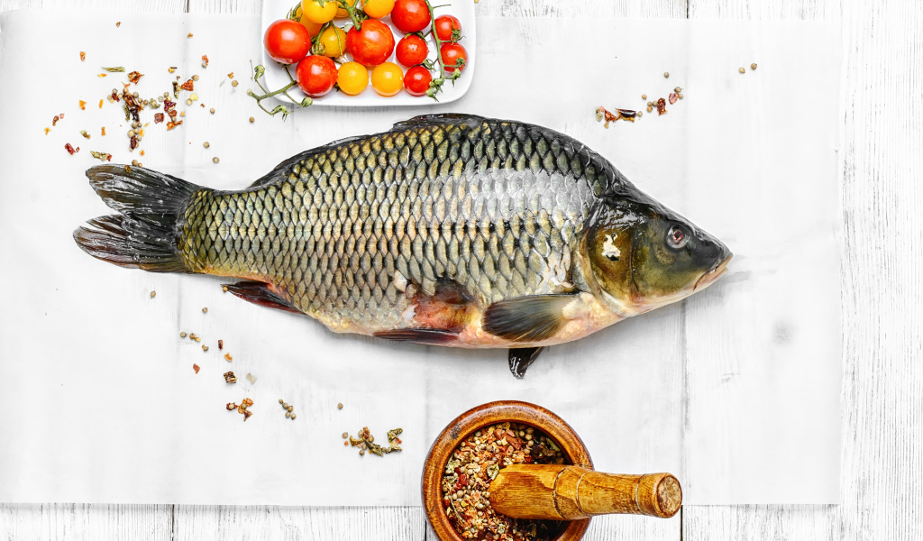 Свежий карась на столе со специями и помидорами