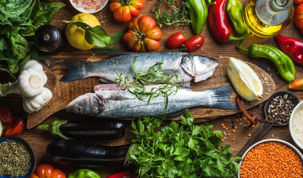 Свежая рыба на столе с овощами и зеленью 