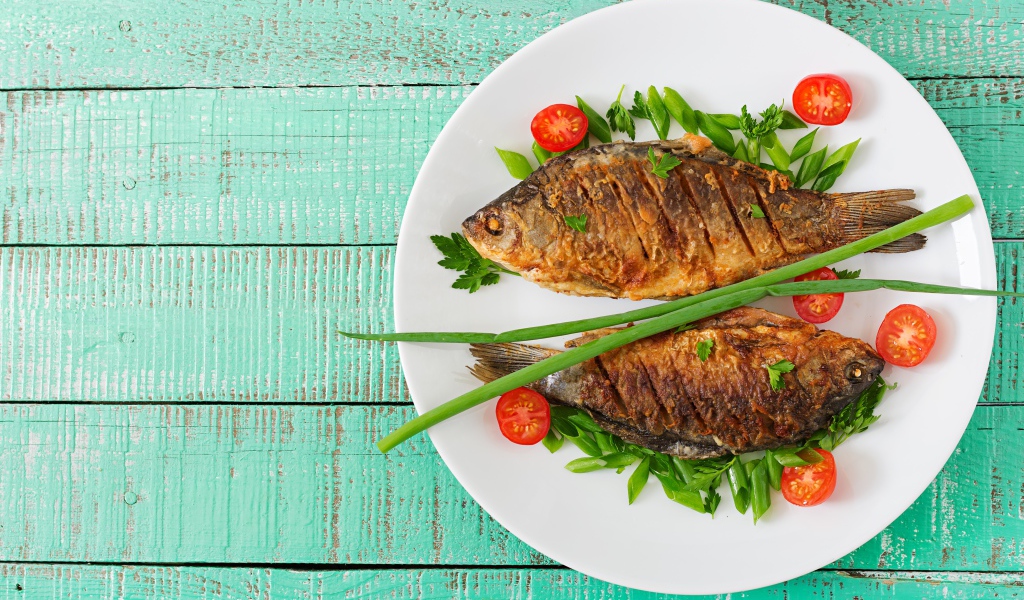 Жареная рыба с помидорами и зеленью на столе