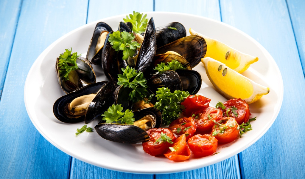 Мидии с томатами, кусочками лимона и зеленью петрушки на белой тарелке