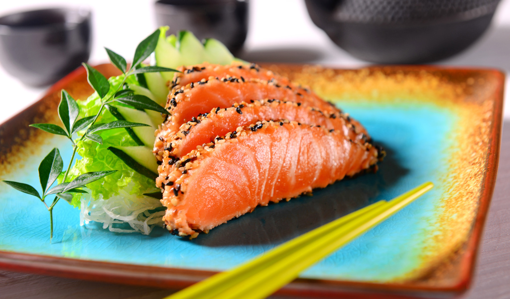 Красная рыба с листьями салата и свежими огурцами на тарелке с палочками