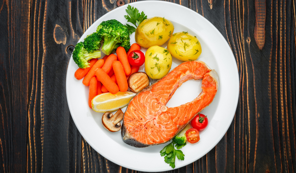 Красная рыба с овощами на белой тарелке на столе