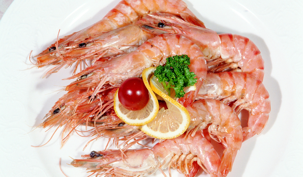 Креветки с лимоном и помидором на белой тарелке