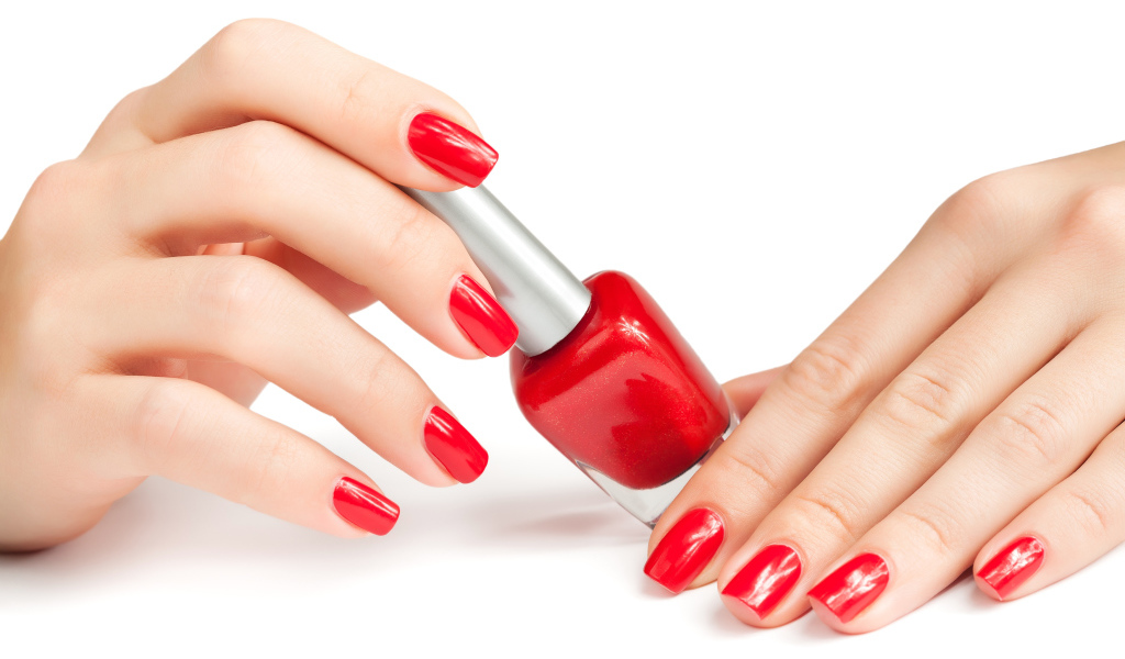 Женские руки с красным маникюром и лаком на белом фоне