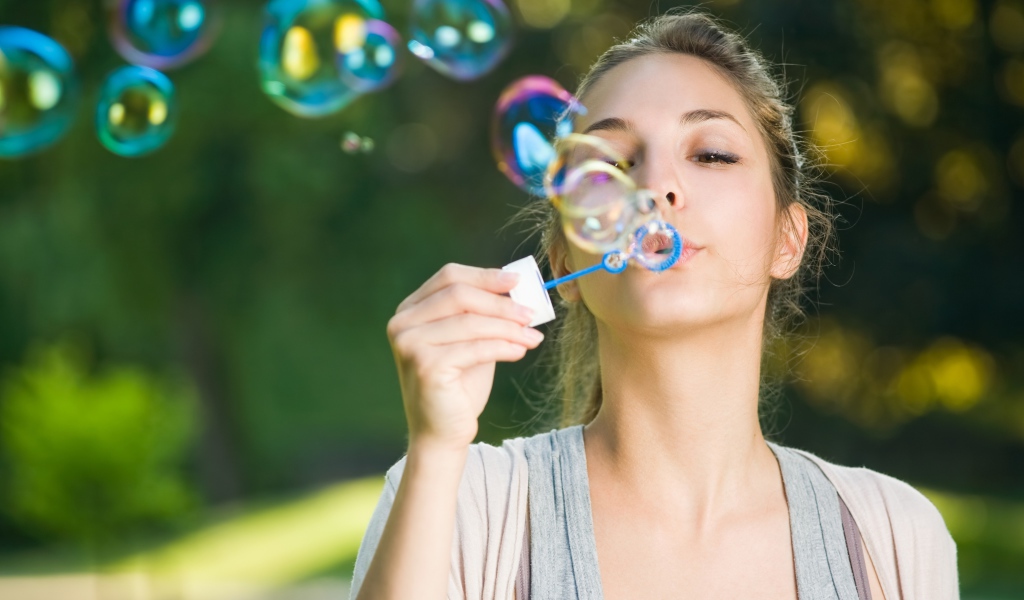 Милая молодая девушка пускает мыльные пузыри