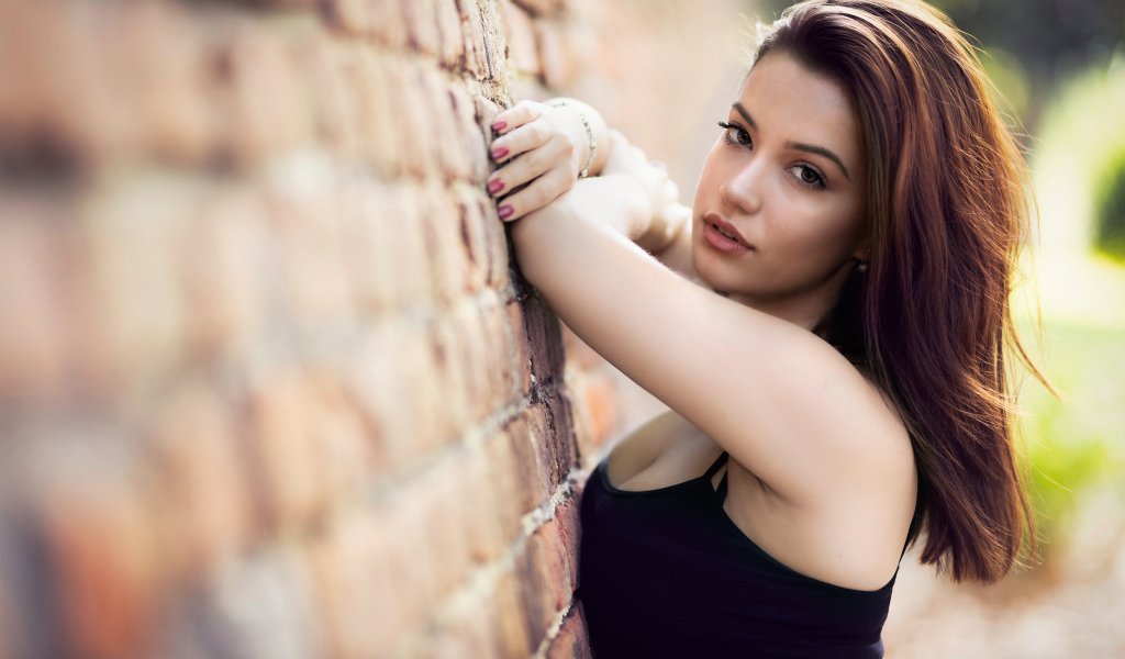 Нежная  девушка шатенка стоит у кирпичной стены