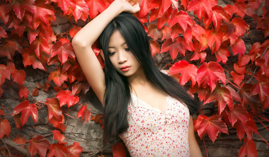 Молодая девушка азиатка стоит у стены с красными листьями