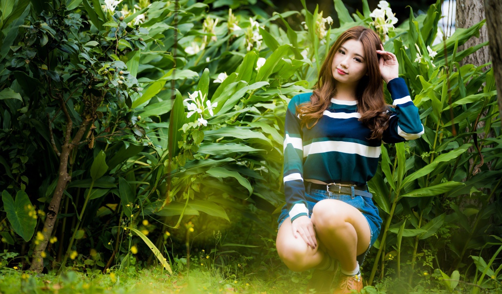 Молодая азиатка сидит в зеленых листьях 