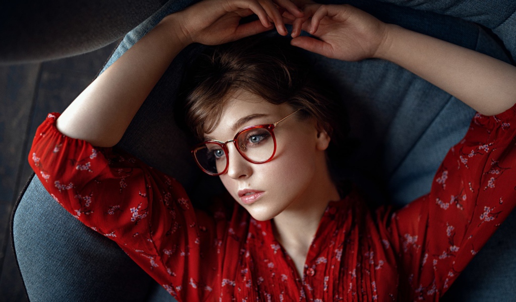 Молодая девушка в очках лежит на диване 