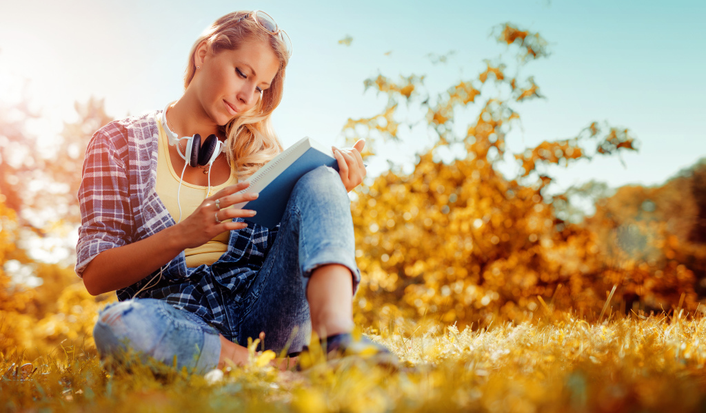Молодая девушка читает книгу на желтой траве осенью