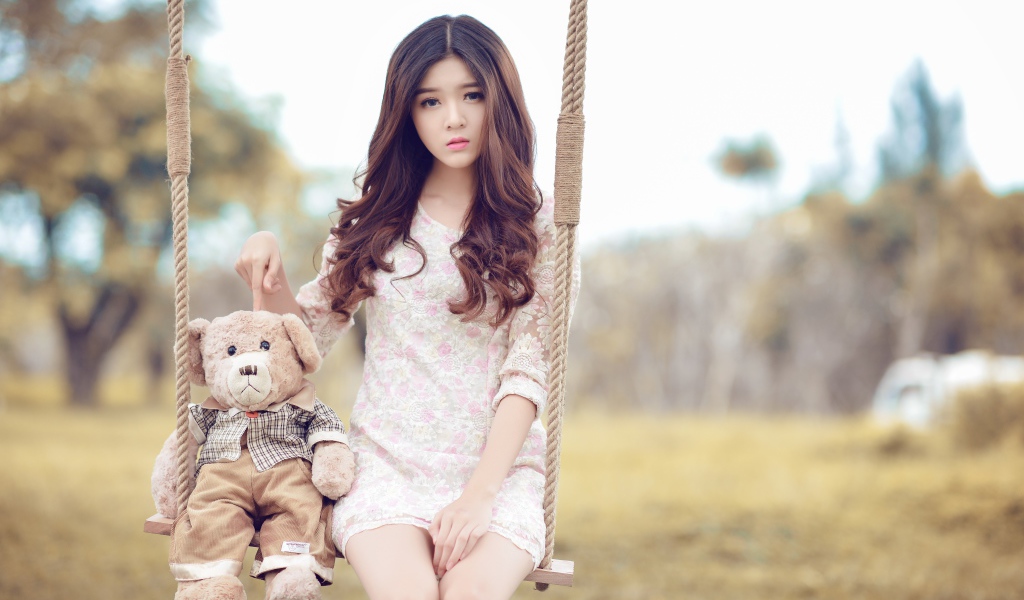 Девочка азиатка сидит на качели с плюшевым мишкой