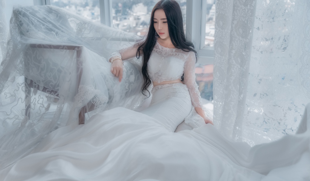 Красивая азиатка в белом свадебном платье сидит на полу