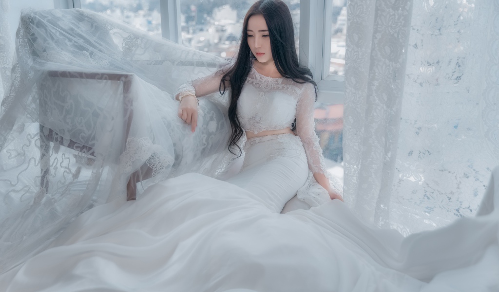 Красивая азиатка в белом свадебном платье сидит на полу