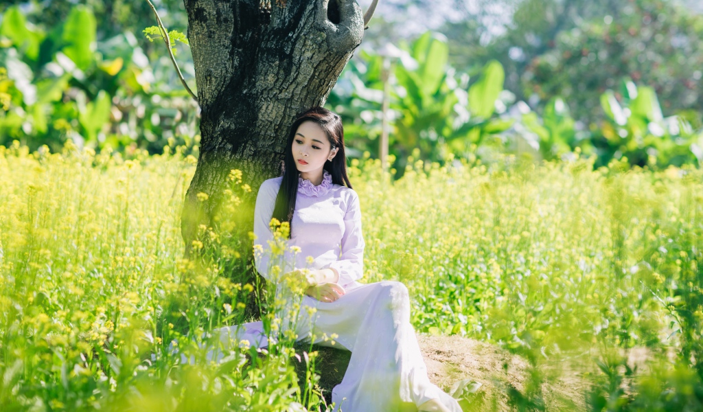 Красивая девушка азиатка сидит в белом платье под деревом