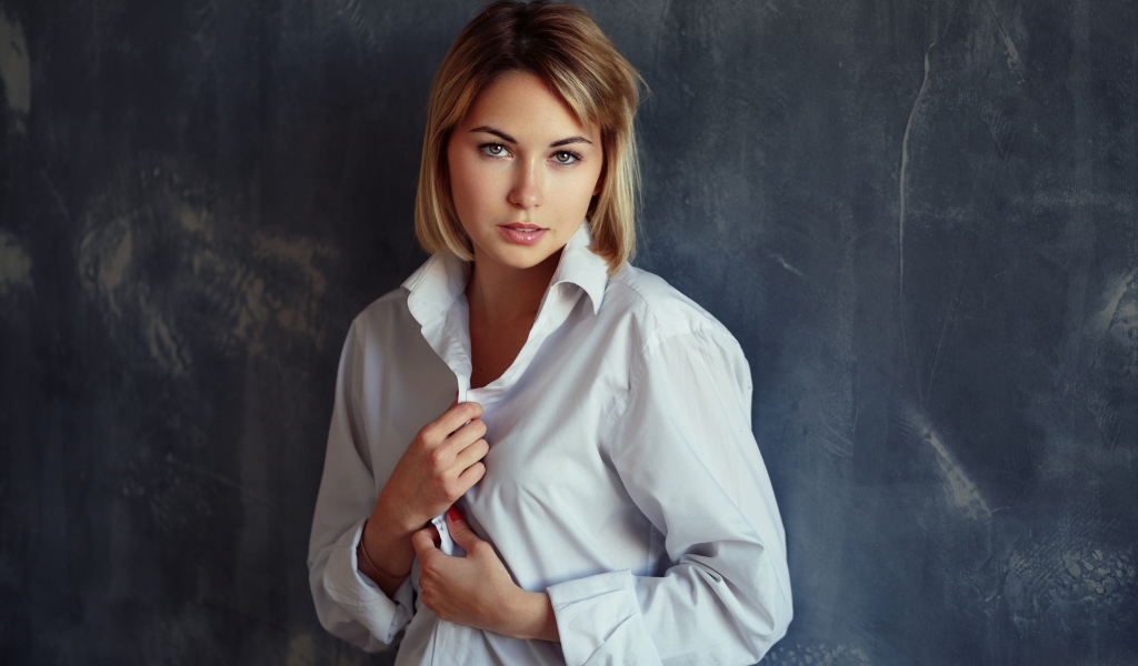 Красивая девушка блондинка в белой рубашке у стены 