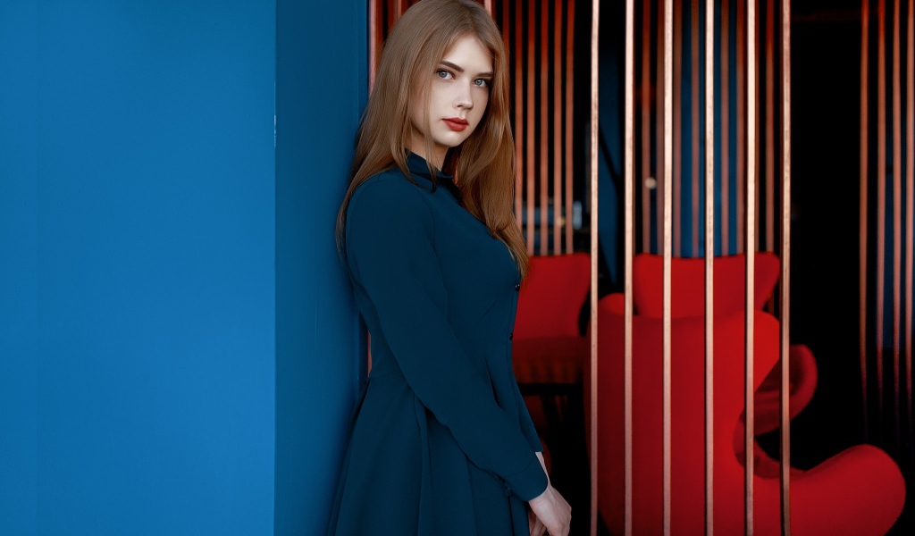 Красивая голубоглазая девушка стоит в пальто у стены