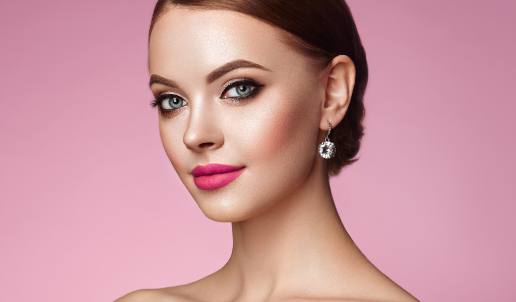 Красивая голубоглазая девушка с красивыми серьгами на розовом фоне