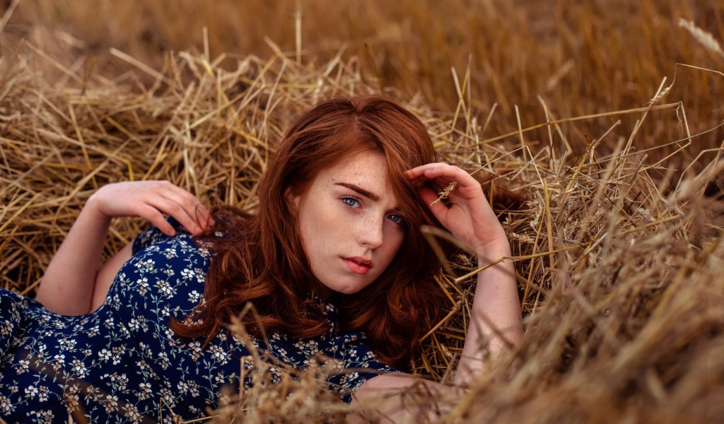 Красивая голубоглазая рыжеволосая девушка лежит в сене