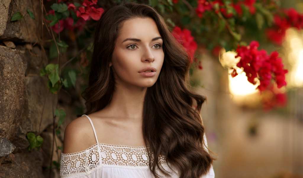 Красивая шатенка у стены на фоне красных цветов