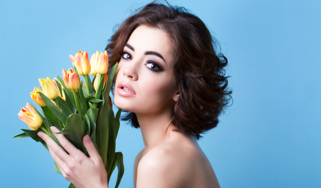 Красивая девушка брюнетка с букетом тюльпанов на голубом фоне