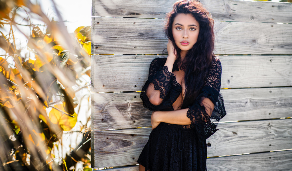 Красивая девушка в черном платье у стены 