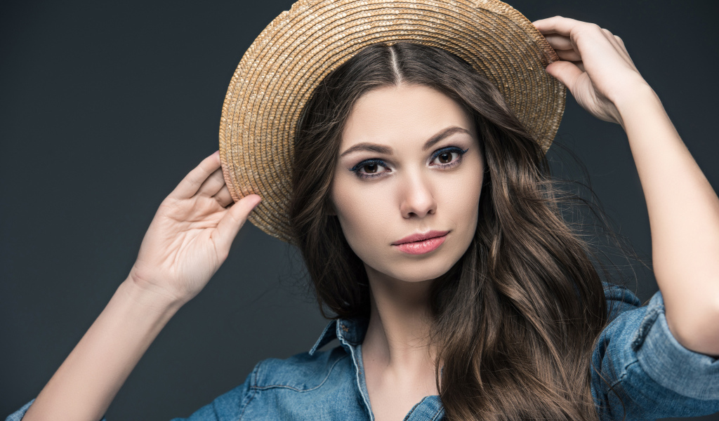 Красивая девушка в соломенной шляпе на сером фоне