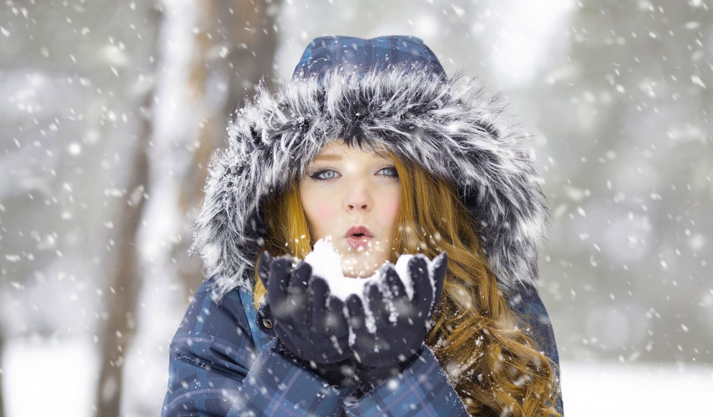 Красивая девушка в теплой куртке со снегом в руках