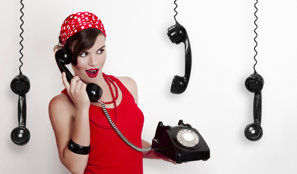 Красивая девушка в красном с черным старым телефоном в руках