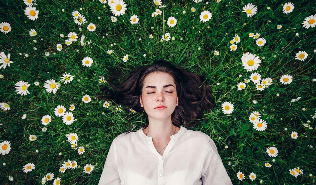 Красивая девушка лежит на зеленой траве с ромашками