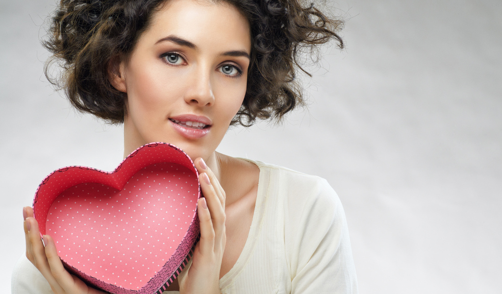 Красивая девушка с коробкой в форме сердца в руках на сером фоне
