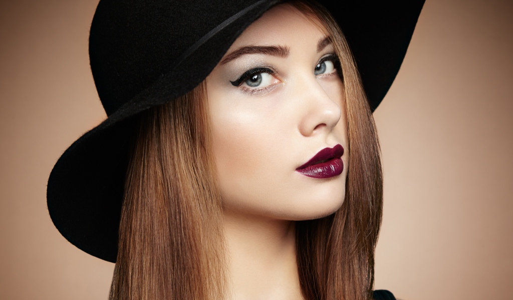 Красивая девушка с ярким макияжем в большой черной шляпе