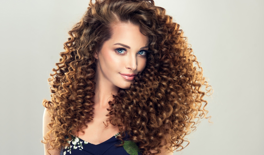 Красивая девушка с длинными волнистыми волосами на сером фоне