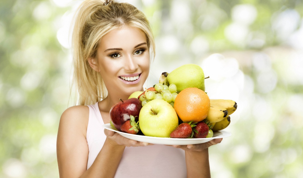 Красивая улыбающаяся блондинка с тарелкой с фруктами в руках