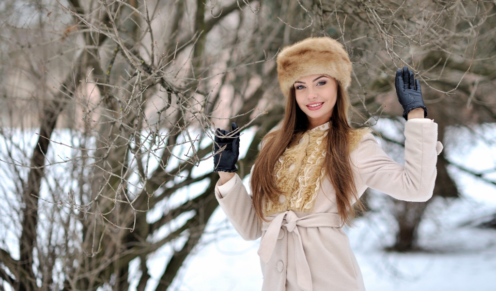 Красивая улыбающаяся девушка в шапке у дерева зимой