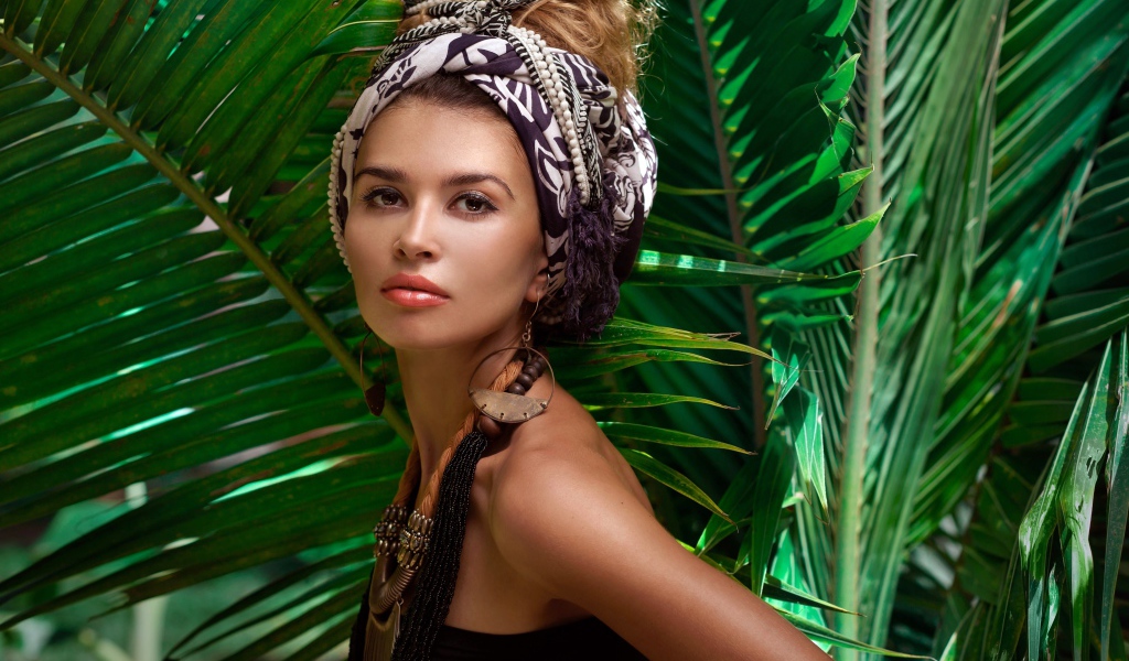 Красивая женщина в тюрбане с украшениями среди зеленых пальмовых листьев
