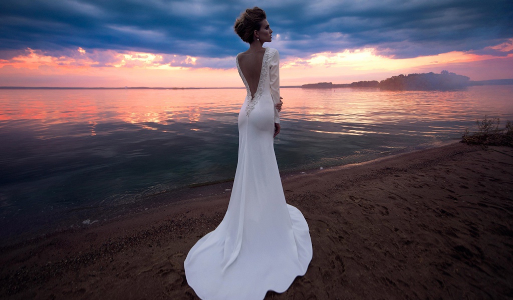 Красивая молодая девушка в свадебном платье у воды на закате 