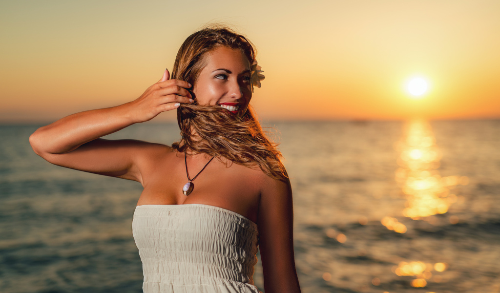 Очаровательная улыбающаяся девушка шатенка на берегу моря на закате
