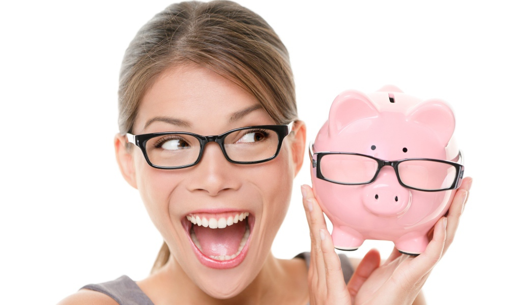 Веселая девушка в очках с копилкой в руках на белом фоне