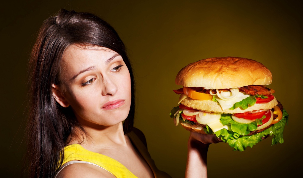 Недовольная девушка с большим гамбургером в руках 