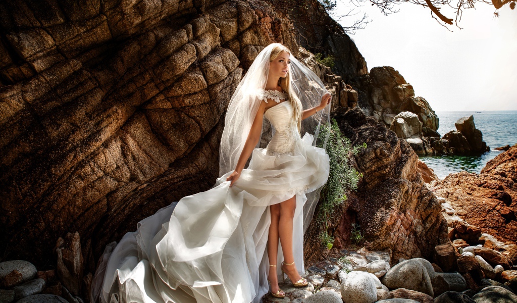 Девушка невеста в белом платье стоит на камнях у скалы