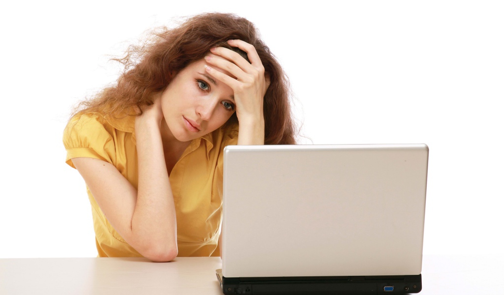 Грустная девушка сидит возле ноутбука 