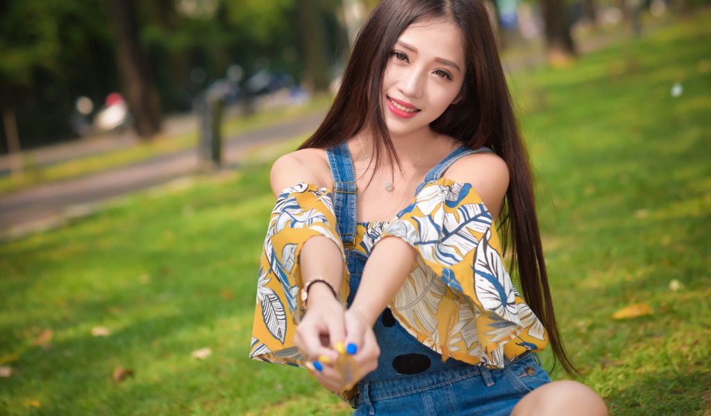 Улыбающаяся девушка азиатка сидит на траве